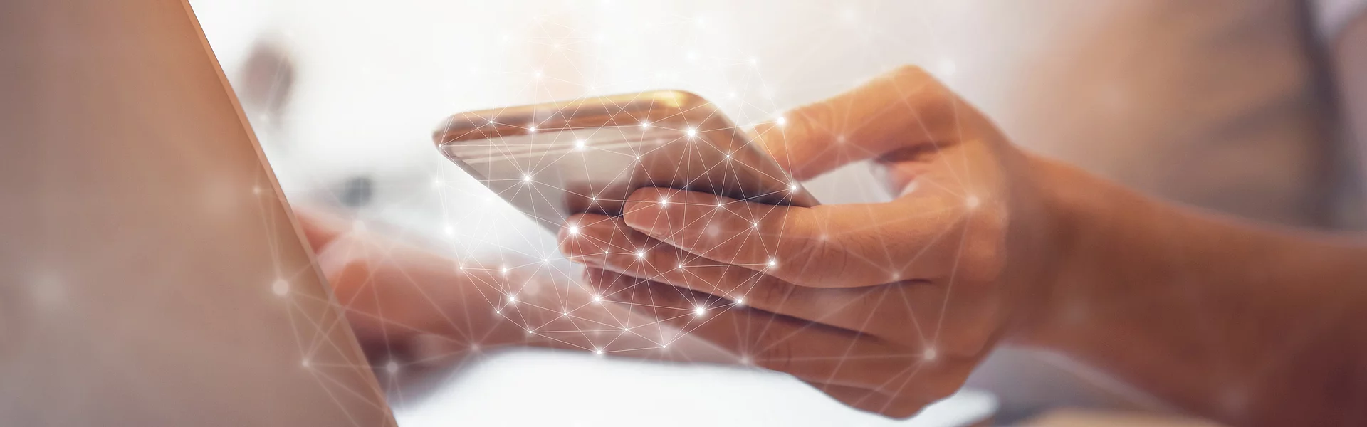 Eine Person tippt auf ein Smartphone; im Hintergrund ein Laptop. Gitterartige Netzwerkverbindungen mit Lichtpunkten überlagern die Szene.