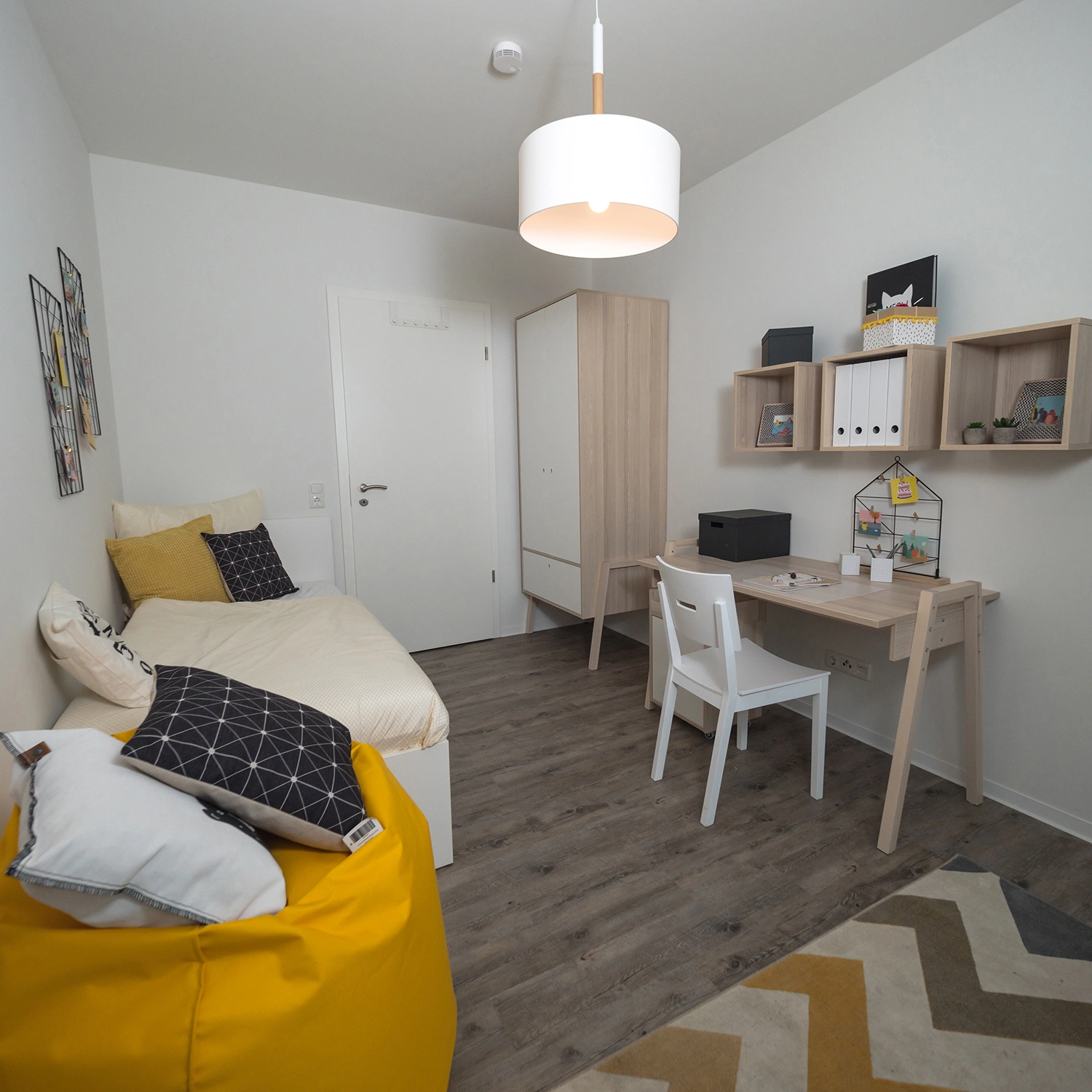 Chambre modulaire meublée avec lit, pouf jaune, bureau et rangements.